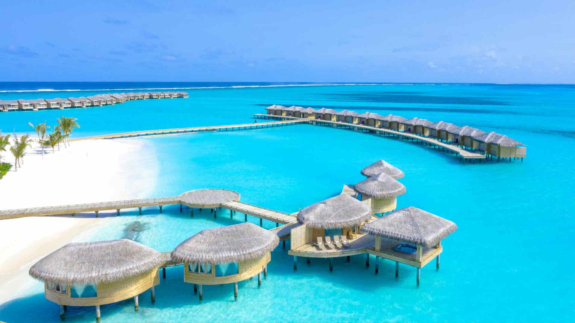 A quiet Caribbean overwater bungalow deck facing a shallow turquoise lagoon, calmer than the open Indian Ocean reef edge