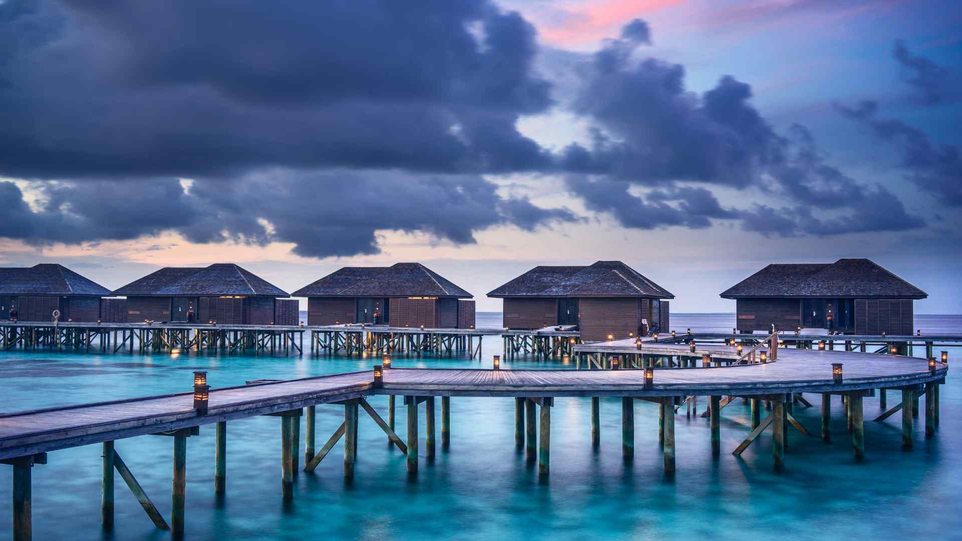Overwater bungalows glowing beside a tropical lagoon at dusk