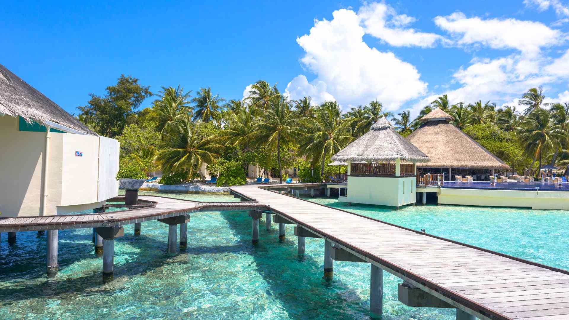 Thatched overwater bungalows on a French Polynesian lagoon with a green volcanic ridge behind them