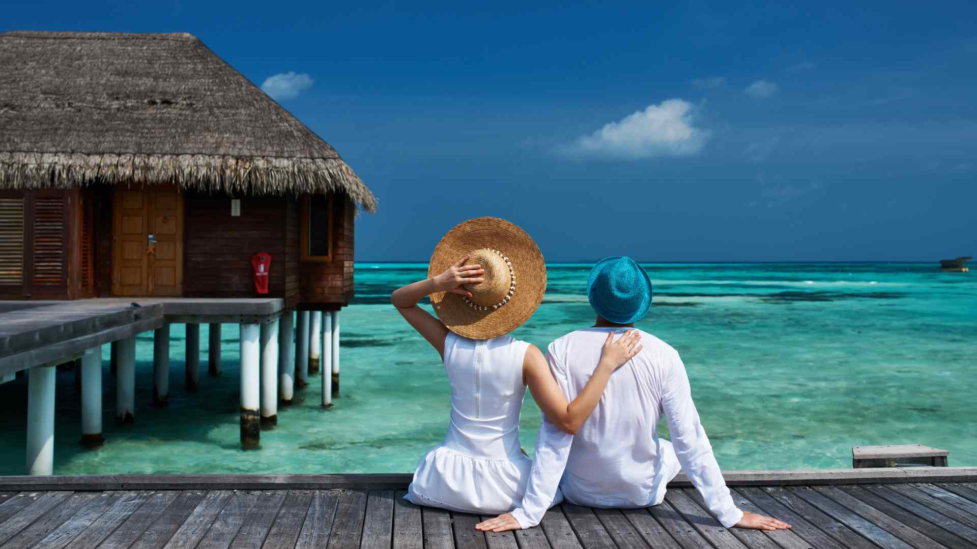 Travelers relaxing on an overwater bungalow deck beside a blue lagoon