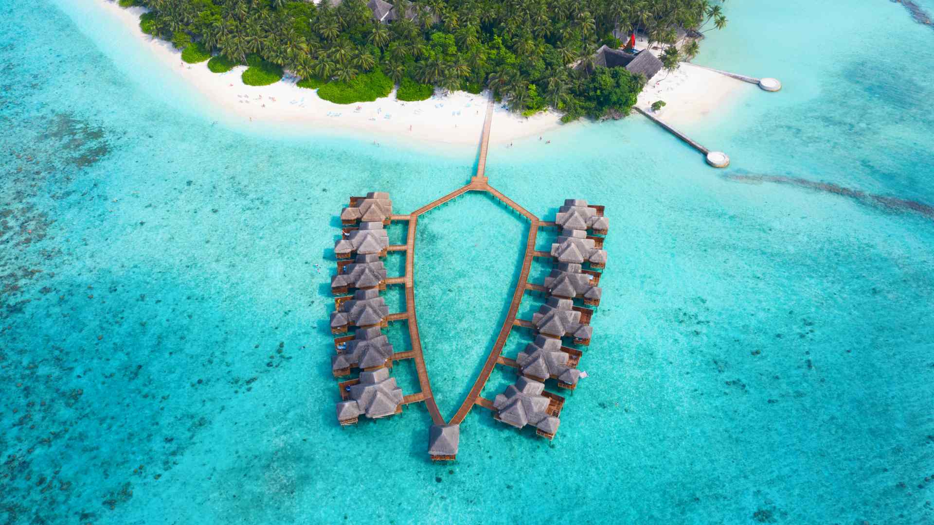 Aerial view of thatched overwater villas beside a tropical Maldives island