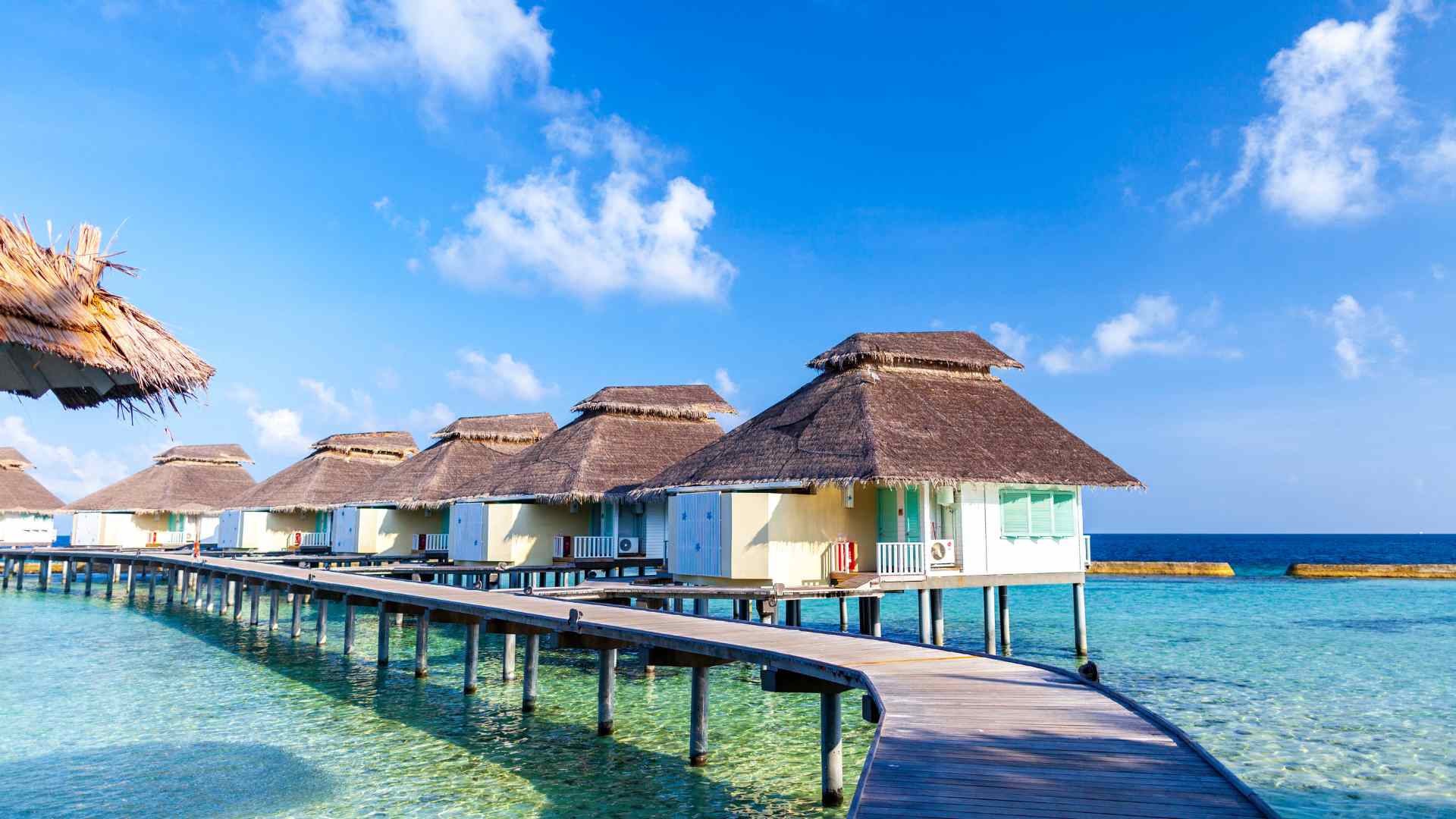 Overwater villas with private sun decks reflected in flat calm water late in the afternoon