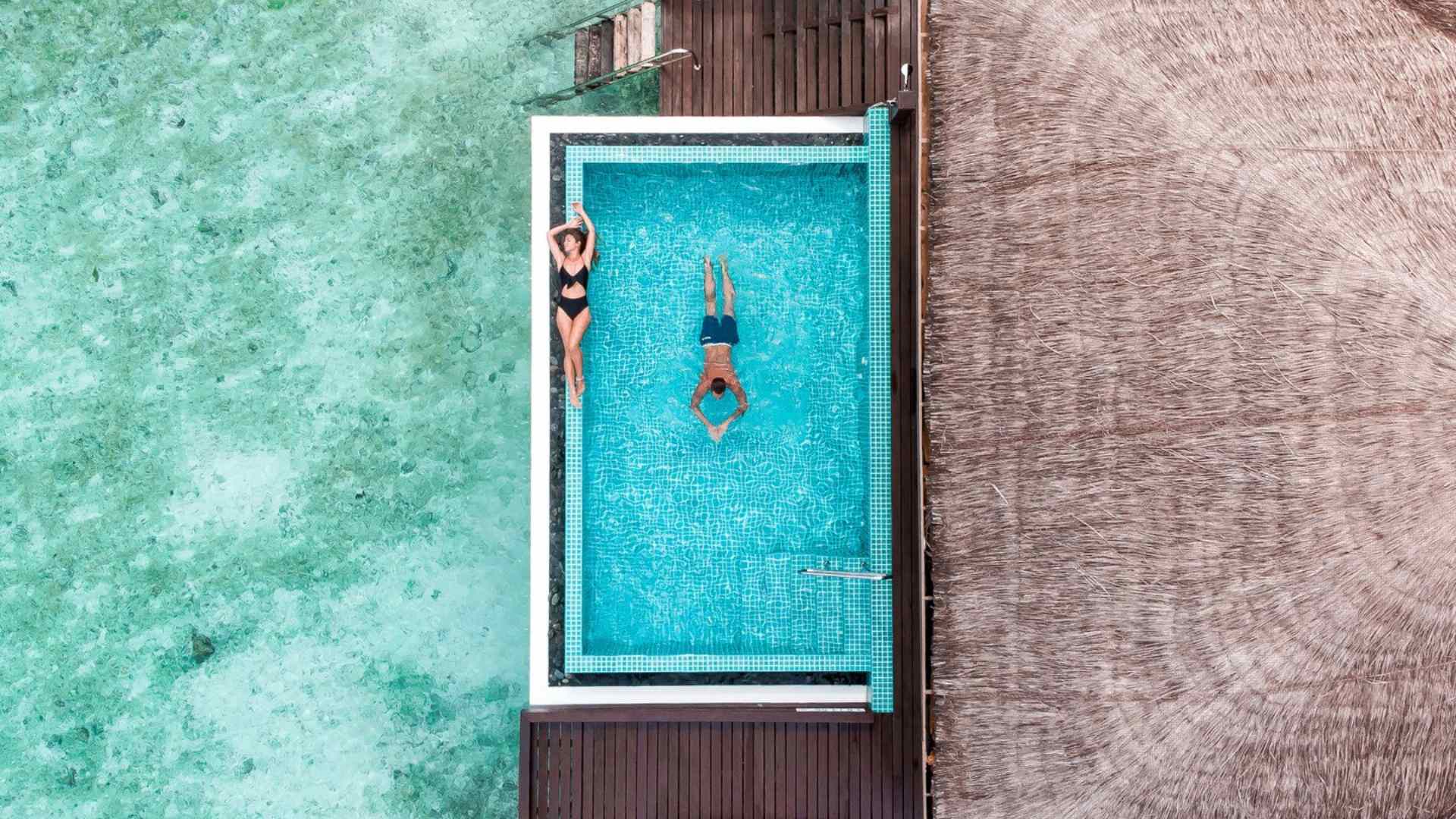 A pair of loungers on a private villa deck facing calm water at golden hour