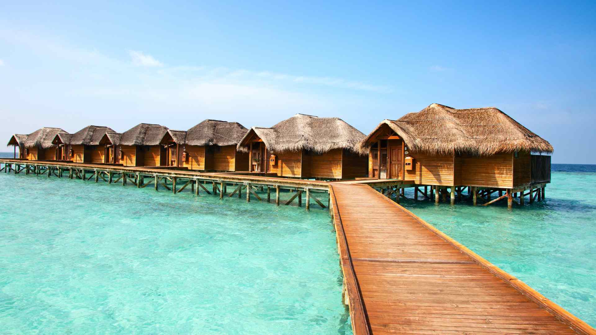 Thatched tropical overwater bungalows connected by a wooden walkway