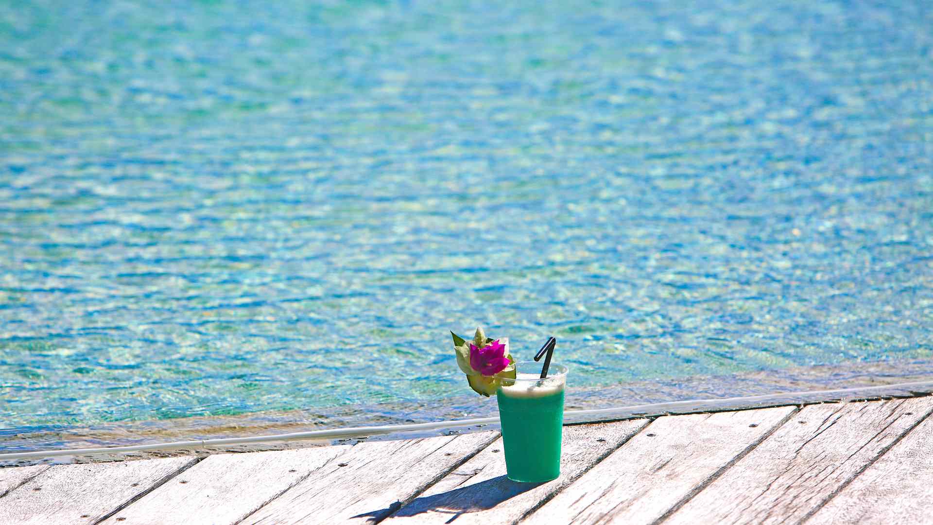 Tropical drink on a wooden deck beside clear lagoon water, shown as general island inspiration